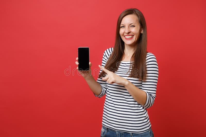 Ritratto della giovane donna graziosa che indica il dito indice sul telefono cellulare con lo schermo vuoto nero dello spazio in fotografie stock Ritratto della giovane donna graziosa che indica il dito indice sul telefono cellulare con lo schermo vuoto nero dello spazio in fotografie stock