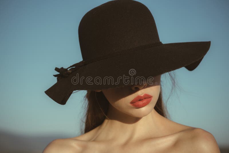 Ritratto di bella donna elegante in un ampio cappello nero sul fondo del cielo blu fotografia stock libera da diritti Ritratto di bella donna elegante in un ampio cappello nero sul fondo del cielo blu fotografia stock libera da diritti