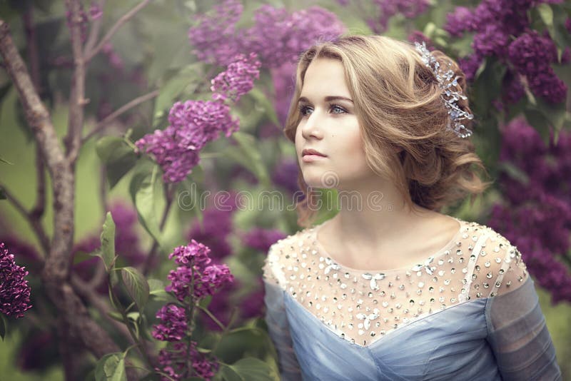Ritratto di bella giovane donna bionda in cespugli lilla, fiori pieni d'ammirazione fotografia stock Ritratto di bella giovane donna bionda in cespugli lilla, fiori pieni d'ammirazione fotografia stock