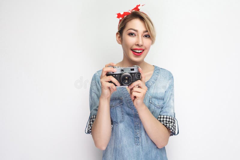 Ritratto di bella giovane donna di blogger in camicia blu casuale del denim con trucco e la condizione rossa della fascia, tenent immagini stock Ritratto di bella giovane donna di blogger in camicia blu casuale del denim con trucco e la condizione rossa della fascia, tenent immagini stock