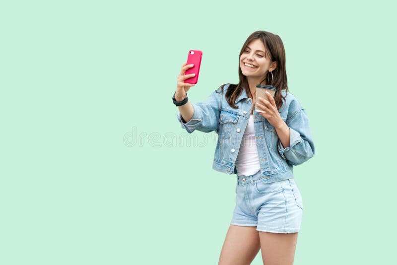 Ritratto di bella giovane donna castana felice nella condizione casuale e nella tenuta di stile del denim smartphone mobile e del fotografie stock libere da diritti Ritratto di bella giovane donna castana felice nella condizione casuale e nella tenuta di stile del denim smartphone mobile e del fotografie stock libere da diritti