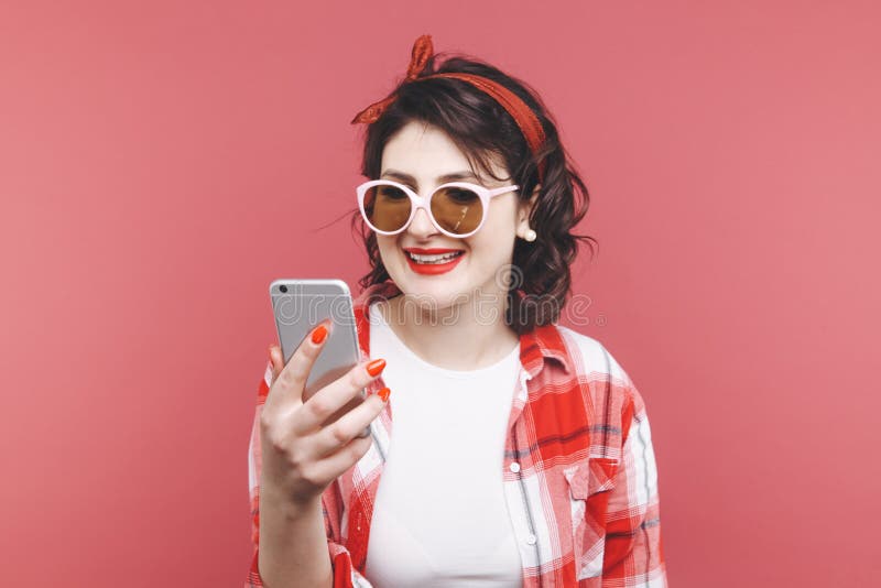 Ritratto di bella ragazza emozionante che porta camicia rossa, giudicante telefono cellulare isolato sopra fondo rosa fotografie stock Ritratto di bella ragazza emozionante che porta camicia rossa, giudicante telefono cellulare isolato sopra fondo rosa fotografie stock