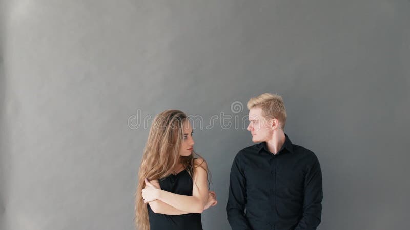 Ritratto di belle giovani coppie, esaminante macchina fotografica e sorridere, stanti contro la parete grigia