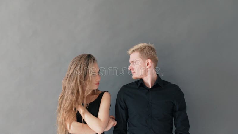 Ritratto di belle giovani coppie, esaminante macchina fotografica e sorridere, stanti contro la parete grigia