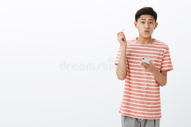 Ritratto di bello giovane adolescente asiatico impressionato che per mezzo di nuove cuffie che decollano earbud per esprimere stu immagini stock