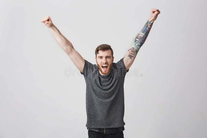 Ritratto di bello uomo caucasico incoraggiante felice con la barba e le mani in aumento tatuate del braccio, gridante nel volume immagini stock Ritratto di bello uomo caucasico incoraggiante felice con la barba e le mani in aumento tatuate del braccio, gridante nel volume immagini stock