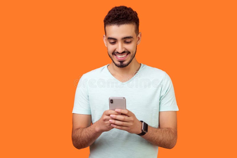 Ritratto di brunetta allegra che usa il cellulare e sorride, che legge buone notizie studio interno isolato sullo sfondo arancion