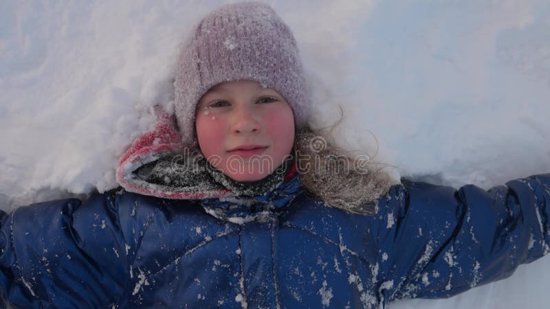 Ritratto di chiusura di una bambina adorabile felice che sorride sdraiata sulla neve. Movimento lento. video d archivio