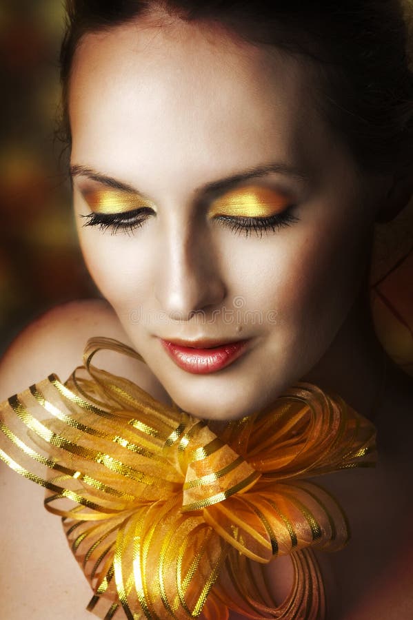 Glamour portrait of young fashion woman face with bright evening golden make up for party and gold ribbon on neck. Concept - make-up as christmas gift. Glamour portrait of young fashion woman face with bright evening golden make up for party and gold ribbon on neck. Concept - make-up as christmas gift