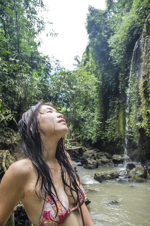 Portrait of young beautiful Asian girl looking pure and enjoying nature beauty with face wet under amazing beautiful natural waterfall in tropical paradise in tourist destination and adventure travel. Portrait of young beautiful Asian girl looking pure and enjoying nature beauty with face wet under amazing beautiful natural waterfall in tropical paradise in tourist destination and adventure travel