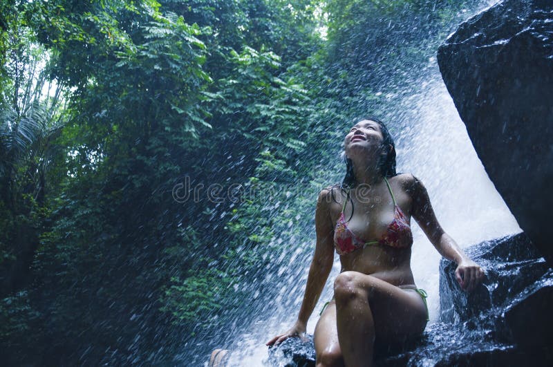 Portrait of young beautiful Asian woman looking pure and enjoying nature beauty with face wet under amazing beautiful natural waterfall in tropical paradise in tourist destination and adventure travel. Portrait of young beautiful Asian woman looking pure and enjoying nature beauty with face wet under amazing beautiful natural waterfall in tropical paradise in tourist destination and adventure travel