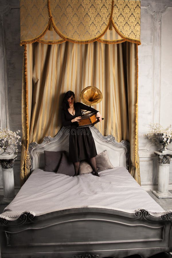 Ritratto di giovane bello modello femminile nella condizione sexy nera del vestito sul letto dentro con lo studio interno del gra fotografia stock libera da diritti Ritratto di giovane bello modello femminile nella condizione sexy nera del vestito sul letto dentro con lo studio interno del gra fotografia stock libera da diritti