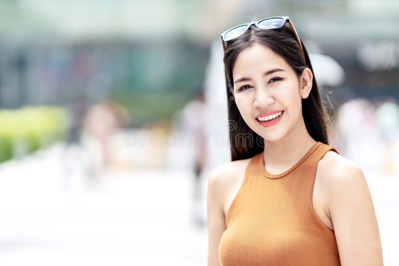 Ritratto di giovane donna asiatica attraente felice che sorride alla macchina fotografica al fondo della città nel concetto dello immagine stock Ritratto di giovane donna asiatica attraente felice che sorride alla macchina fotografica al fondo della città nel concetto dello immagine stock