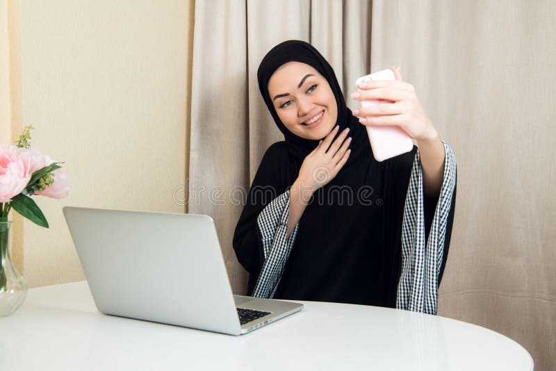 Ritratto di giovane donna attraente nel hijab che fa la foto del selfie sullo smartphone immagine stock libera da diritti Ritratto di giovane donna attraente nel hijab che fa la foto del selfie sullo smartphone immagine stock libera da diritti