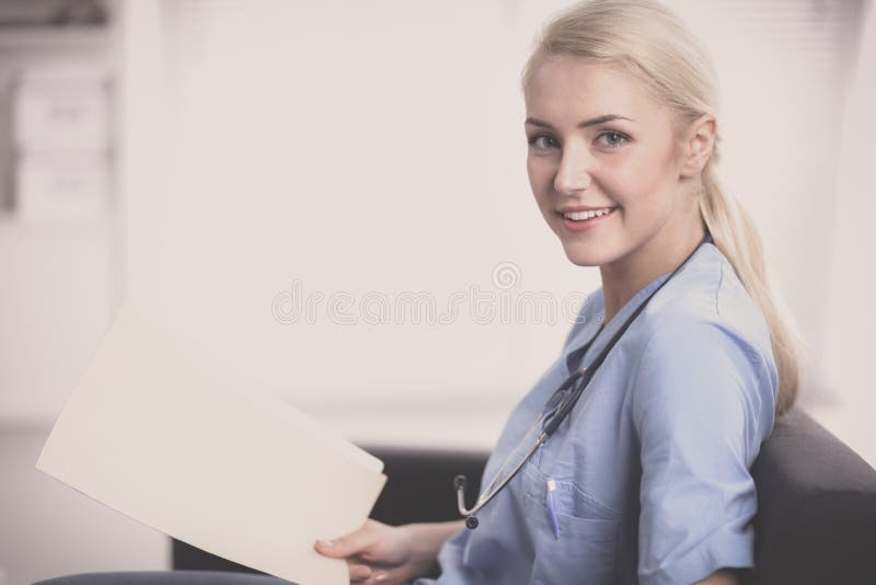 Ritratto di giovane medico felice che si siede sul sofà con la cartella fotografia stock Ritratto di giovane medico felice che si siede sul sofà con la cartella fotografia stock