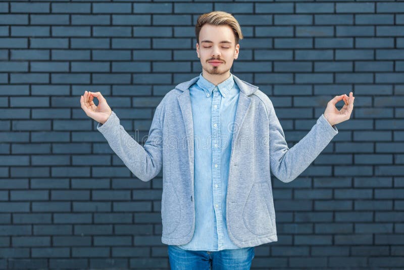 Ritratto di giovane uomo biondo bello serio calmo nello stile casuale che sta nella posa di yoga, negli occhi chiusi e nella medi fotografia stock libera da diritti Ritratto di giovane uomo biondo bello serio calmo nello stile casuale che sta nella posa di yoga, negli occhi chiusi e nella medi fotografia stock libera da diritti