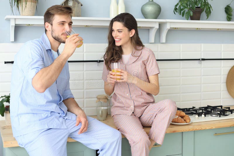 Ritratto di giovani coppie felici in pigiami che cucinano insieme nella cucina, succo d'arancia bevente di mattina a casa fotografie stock Ritratto di giovani coppie felici in pigiami che cucinano insieme nella cucina, succo d'arancia bevente di mattina a casa fotografie stock