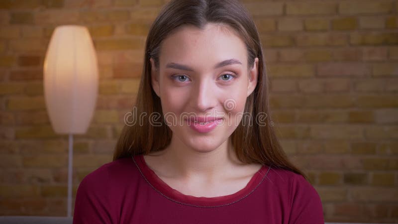 Ritratto di giovani e bei sorrisi femminili castana piacevolmente nella macchina fotografica nella casa