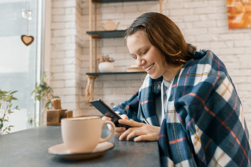 Ritratto di inverno di autunno della ragazza teenager sorridente con il telefono cellulare e la tazza di caffè in caffetteria, ra immagini stock libere da diritti Ritratto di inverno di autunno della ragazza teenager sorridente con il telefono cellulare e la tazza di caffè in caffetteria, ra immagini stock libere da diritti