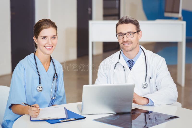 Ritratto di medici sorridenti che si siedono allo scrittorio fotografia stock libera da diritti Ritratto di medici sorridenti che si siedono allo scrittorio fotografia stock libera da diritti