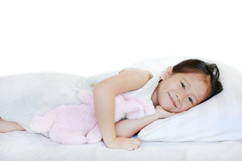 Ritratto di piccola ragazza asiatica sorridente dolce che si trova sul letto di mattina con l'esame della macchina fotografica fotografia stock libera da diritti Ritratto di piccola ragazza asiatica sorridente dolce che si trova sul letto di mattina con l'esame della macchina fotografica fotografia stock libera da diritti