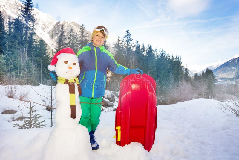 Ritratto di ragazzo con pupazzo di neve, slitta in montagna fotografie stock libere da diritti Ritratto di ragazzo con pupazzo di neve, slitta in montagna fotografie stock libere da diritti