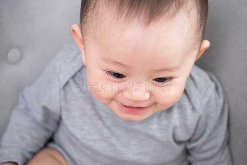Ritratto di risata sorridente adorabile sveglia, neonata del primo piano con gli occhi neri che si siedono sul sof? che guarda a immagini stock Ritratto di risata sorridente adorabile sveglia, neonata del primo piano con gli occhi neri che si siedono sul sof? che guarda a immagini stock