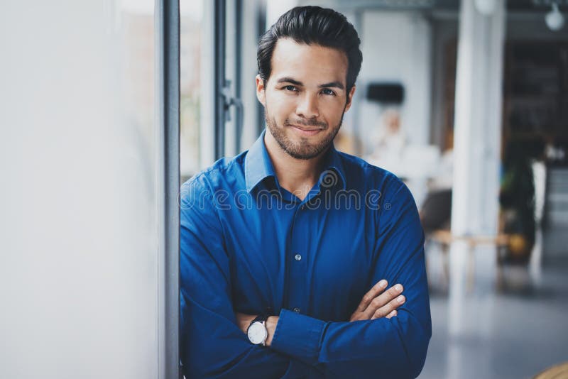 Ritratto di riuscito uomo d'affari ispanico sicuro che sorride e che sta vicino dalla finestra in ufficio moderno fotografie stock libere da diritti Ritratto di riuscito uomo d'affari ispanico sicuro che sorride e che sta vicino dalla finestra in ufficio moderno fotografie stock libere da diritti