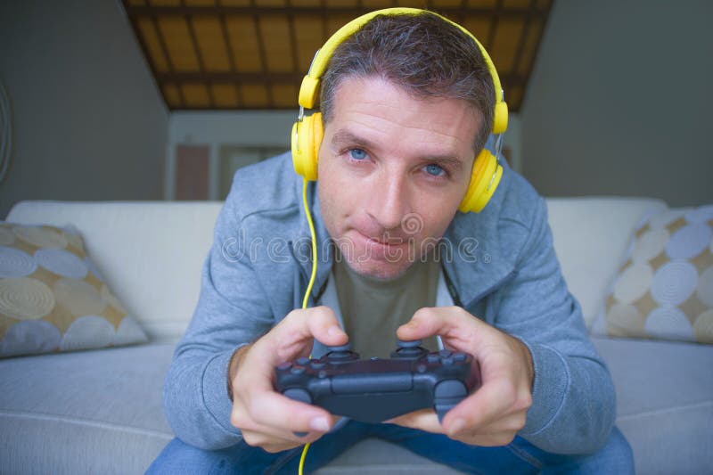 Lifestyle portrait of young happy and excited gamer man with headphones playing video game at home having fun on sofa couch holding controller concentrated in gaming concept. Lifestyle portrait of young happy and excited gamer man with headphones playing video game at home having fun on sofa couch holding controller concentrated in gaming concept