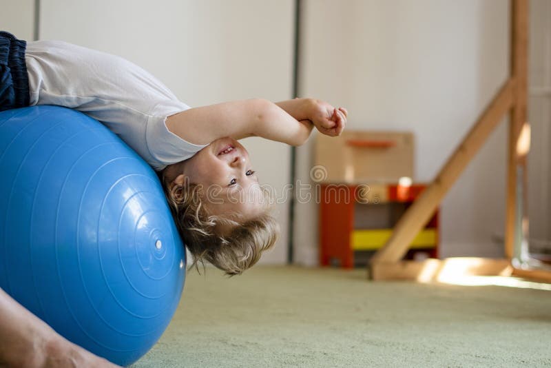 Portrait of a child with cerebral palsy on physiotherapy in a children therapy center. Boy with disability has therapy by doing exercises. Special needs kid has therapy with physiotherapist. Portrait of a child with cerebral palsy on physiotherapy in a children therapy center. Boy with disability has therapy by doing exercises. Special needs kid has therapy with physiotherapist