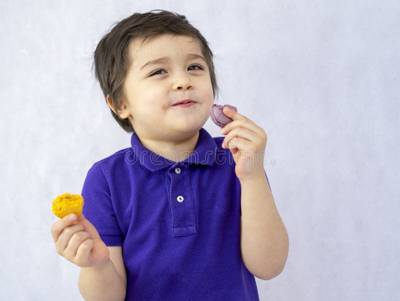 Ritratto di un bambino felice che mangia macarone su sfondo bianco, sorridente bambino che apprezza il suo dolce spuntino piccolo fotografia stock