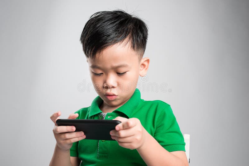 Ritratto di un bambino sveglio divertente che gioca sullo smartphone isolato sopra fondo grigio fotografie stock Ritratto di un bambino sveglio divertente che gioca sullo smartphone isolato sopra fondo grigio fotografie stock