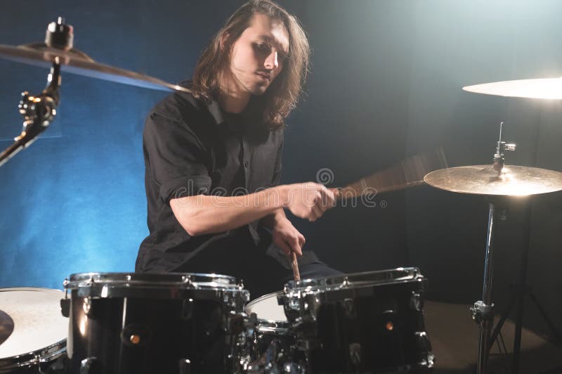 Portrait of a long-haired drummer with chopsticks in his hands sitting behind a drum set. Low key. Concepts of the creative freedom of the millenial generation. Portrait of a long-haired drummer with chopsticks in his hands sitting behind a drum set. Low key. Concepts of the creative freedom of the millenial generation.