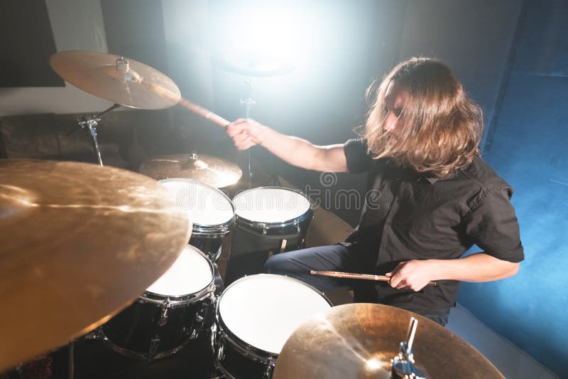 Portrait of a long-haired drummer with chopsticks in his hands sitting behind a drum set. Low key. Concepts of the creative freedom of the millenial generation. Portrait of a long-haired drummer with chopsticks in his hands sitting behind a drum set. Low key. Concepts of the creative freedom of the millenial generation.