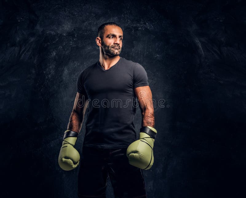 Ritratto di un combattente professionale brutale in una camicia nera ed in guanti Foto dello studio contro una parete strutturata fotografia stock Ritratto di un combattente professionale brutale in una camicia nera ed in guanti Foto dello studio contro una parete strutturata fotografia stock