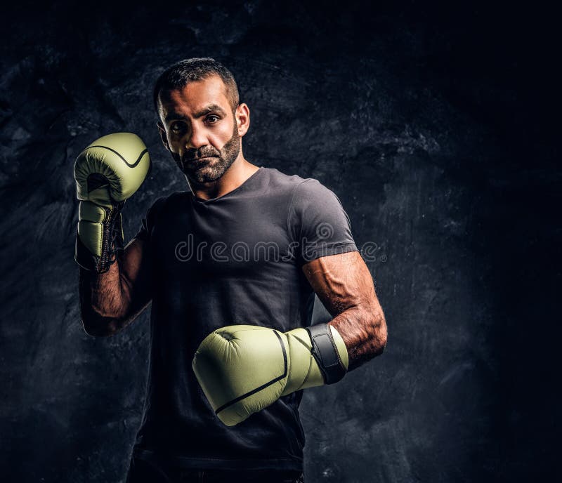 Ritratto di un combattente professionale brutale in una camicia nera ed in guanti Foto dello studio contro una parete strutturata immagini stock Ritratto di un combattente professionale brutale in una camicia nera ed in guanti Foto dello studio contro una parete strutturata immagini stock