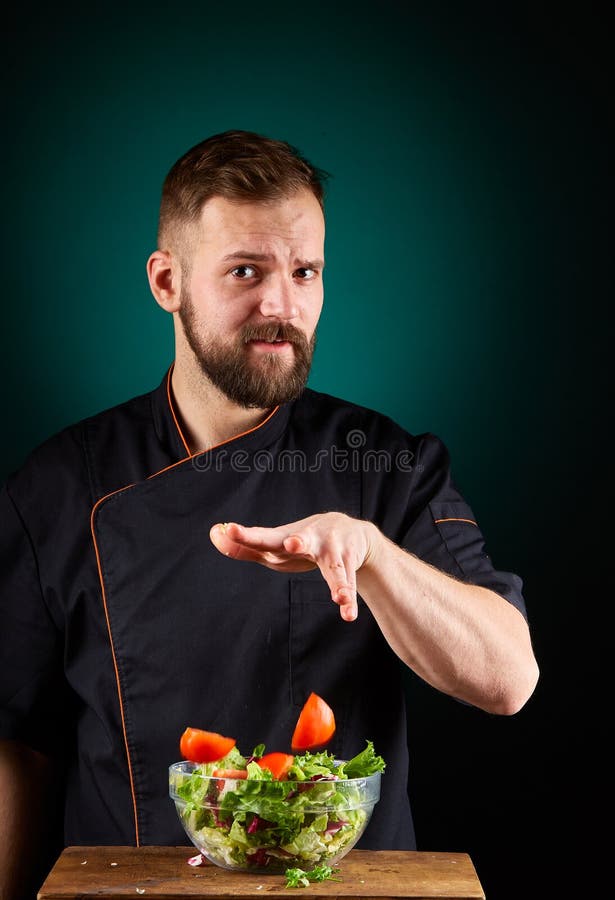 Ritratto di un cuoco maschio bello del cuoco unico che produce insalata saporita su un fondo vago dell'acquamarina fotografia stock Ritratto di un cuoco maschio bello del cuoco unico che produce insalata saporita su un fondo vago dell'acquamarina fotografia stock