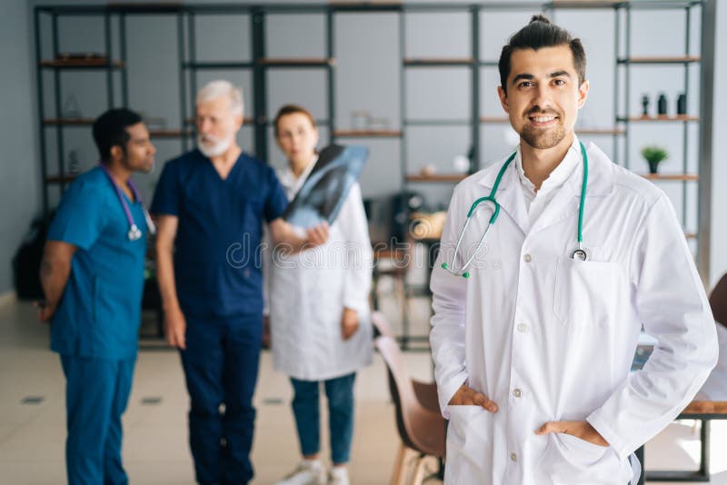 Ritratto di un giovane e allegro medico con l'uniforme bianca in piedi all'ufficio di riunione medica che guarda la telecamera. fotografie stock