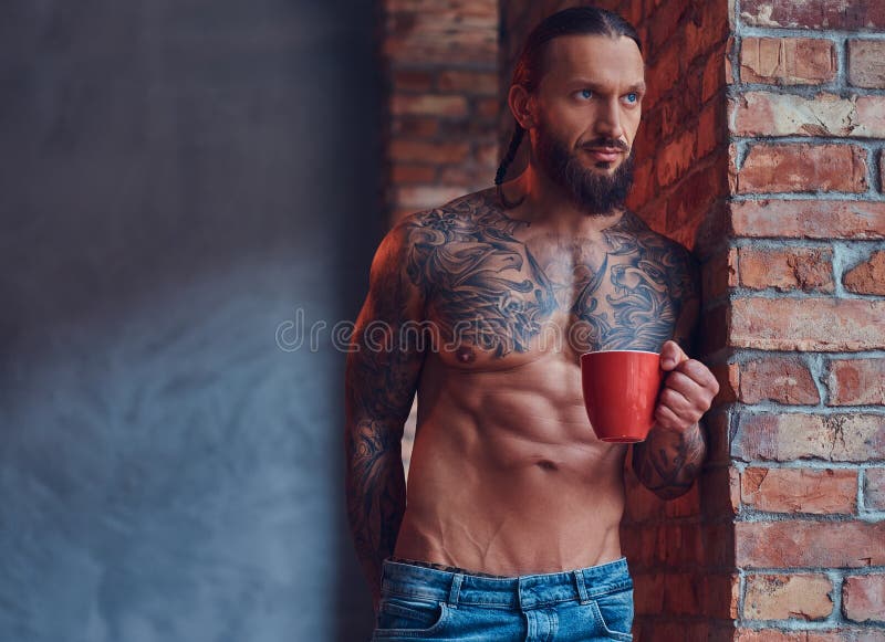 Ritratto di un maschio senza camicia tattoed con un taglio di capelli e una barba alla moda, caffè di mattina delle bevande, pend immagini stock libere da diritti Ritratto di un maschio senza camicia tattoed con un taglio di capelli e una barba alla moda, caffè di mattina delle bevande, pend immagini stock libere da diritti