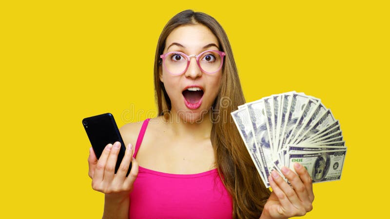 Ritratto di un mazzo emozionante di rappresentazione della giovane donna di banconote dei soldi e di telefono cellulare di tenuta fotografie stock libere da diritti Ritratto di un mazzo emozionante di rappresentazione della giovane donna di banconote dei soldi e di telefono cellulare di tenuta fotografie stock libere da diritti