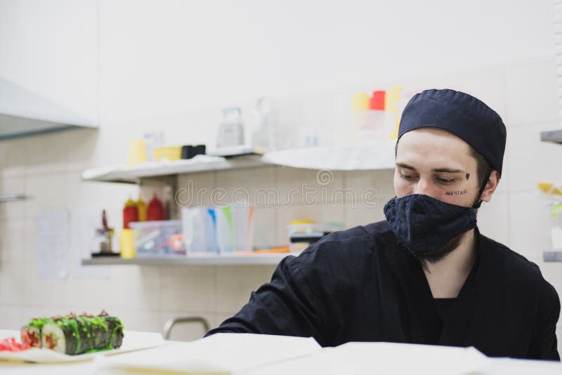 Ritratto di un sushi chef che indossa mascherine nella cucina commerciale. immagini stock libere da diritti