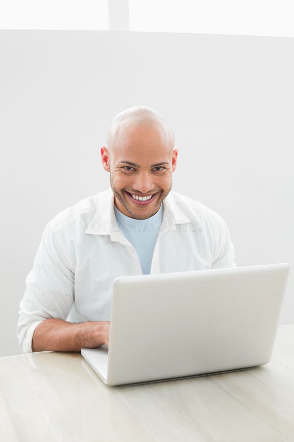 Ritratto di un uomo sorridente casuale che per mezzo del computer portatile allo scrittorio immagine stock libera da diritti Ritratto di un uomo sorridente casuale che per mezzo del computer portatile allo scrittorio immagine stock libera da diritti