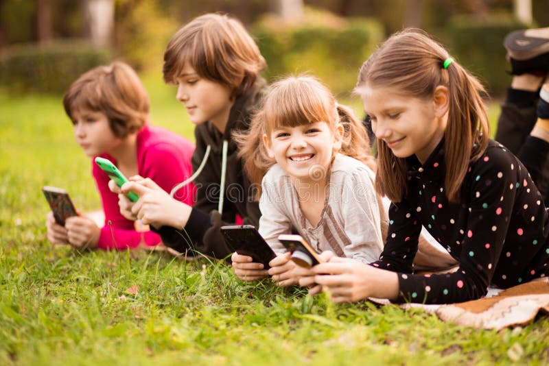 Ritratto di una bambina sorridente che usa il cellulare e si stende con gli amici sull'erba al parco immagini stock libere da diritti