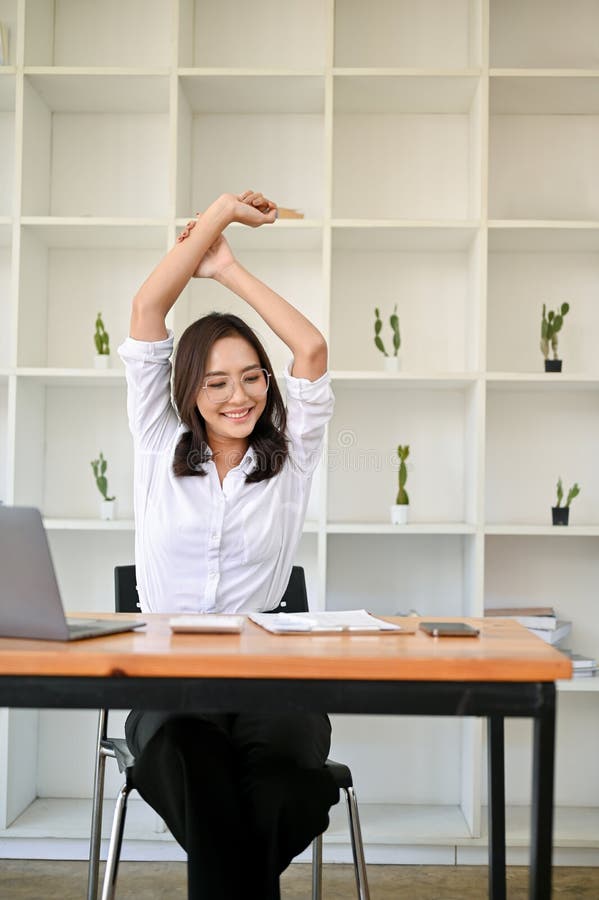 Ritratto di una donna d'affari asiatica positiva che si rilassava e allungava le braccia sulla scrivania del suo ufficio fotografie stock