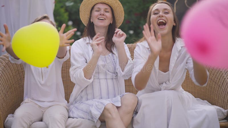 Ritratto di una donna incinta gioiosa e di ragazze carine che guardano una telecamera che lancia palloncini colorati a forma di cu archivi video