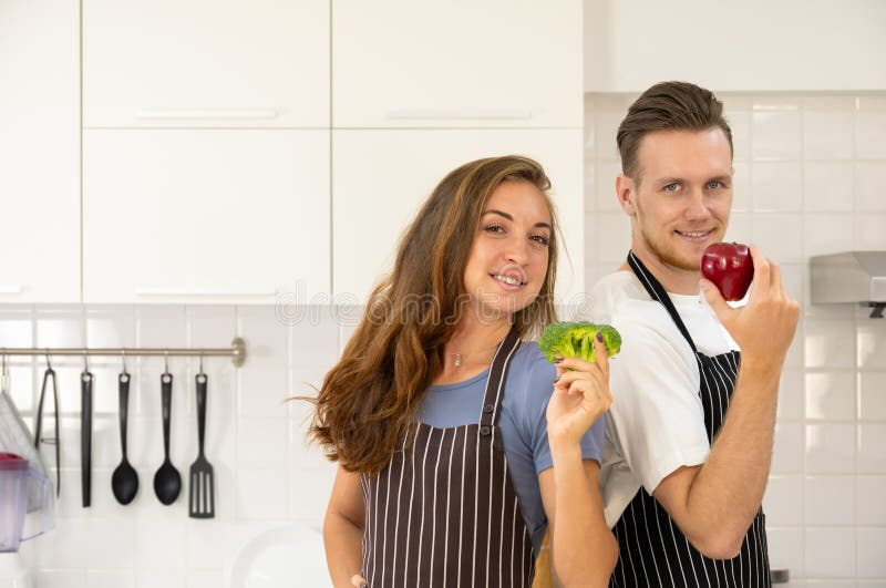 Ritratto di una coppia/famiglia sorridente e affettuosa in piedi in cucina. L'uomo tiene in mano una mela mentre la donna tiene in fotografie stock