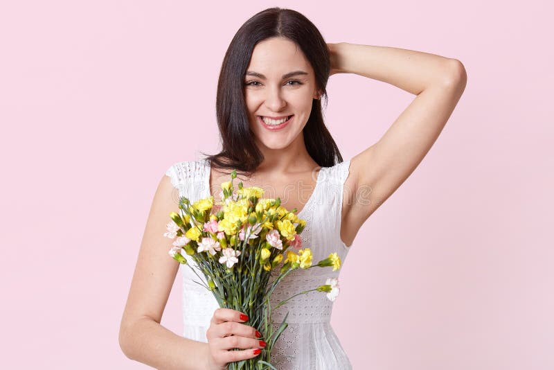 Ritratto di una giovane donna allegra felice in vestito bianco da estate che tiene i fiori colourful in una mano, riparando i suo fotografia stock Ritratto di una giovane donna allegra felice in vestito bianco da estate che tiene i fiori colourful in una mano, riparando i suo fotografia stock