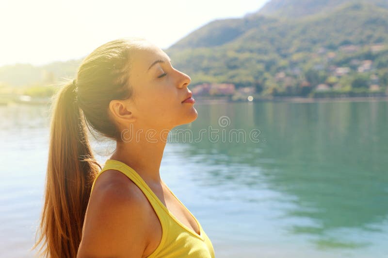 Ritratto di una giovane donna che respira profondamente all'aperto sul lago con un'imprecazione sportiva, testa in su, occhi chiu