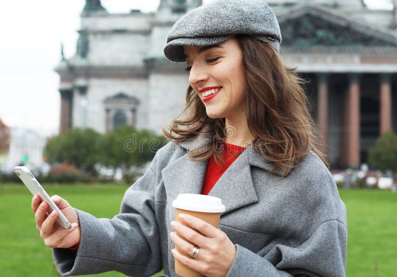 Ritratto di una giovane donna che usa il cellulare mentre tiene in mano una tazza di caffè per strada. fotografie stock libere da diritti