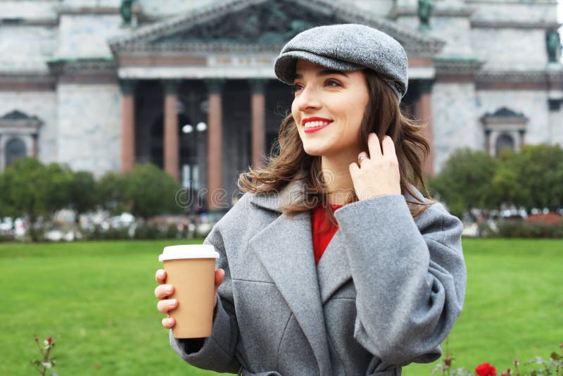 Ritratto di una giovane donna che usa il cellulare mentre tiene in mano una tazza di caffè per strada. immagini stock